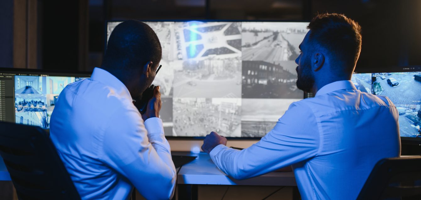 Two male security guards looking at computer screen while one of them explaining detail of video