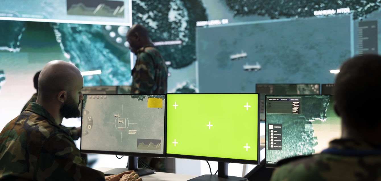 Army soldier working with an isolated pc display next to satellite footage