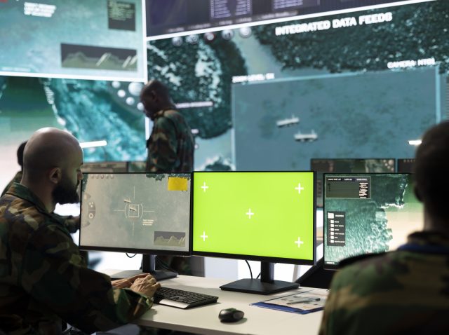 Army soldier working with an isolated pc display next to satellite footage