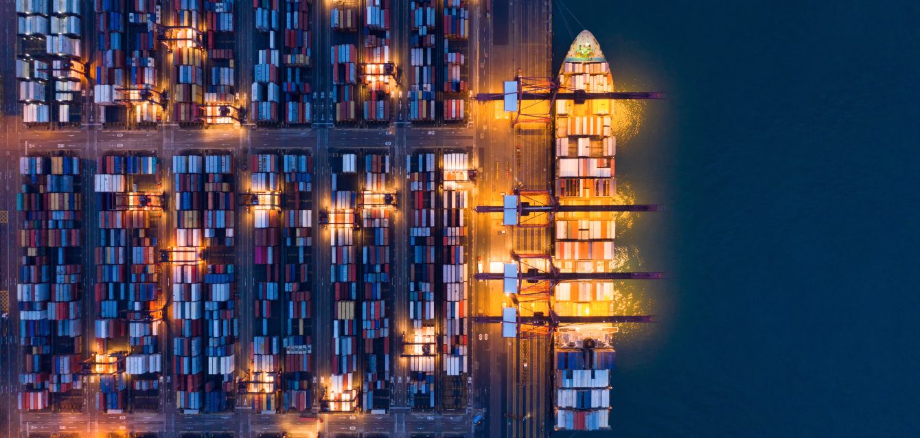Aerial top view of container cargo ship in the export and import business and logistics international goods in urban city. Shipping to the harbor by crane in Victoria Harbour, Hong Kong City at night.