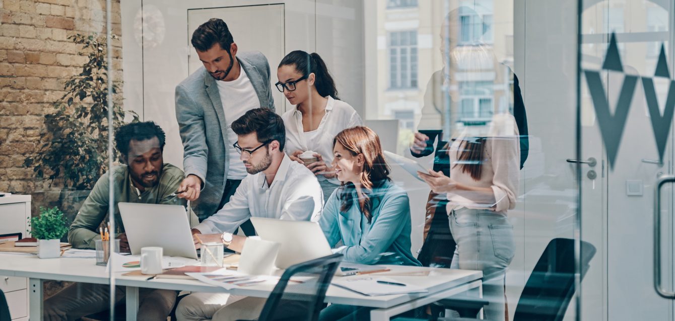 Group of young modern people in smart casual wear communicating and using modern technologies while working in the office