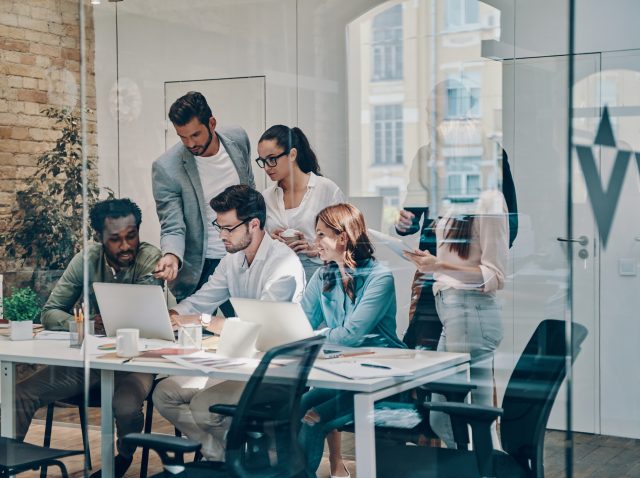 Group of young modern people in smart casual wear communicating and using modern technologies while working in the office