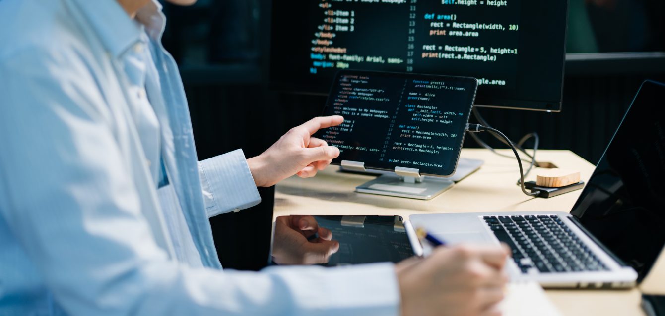 Asian software developer working late with code on screens, tabl