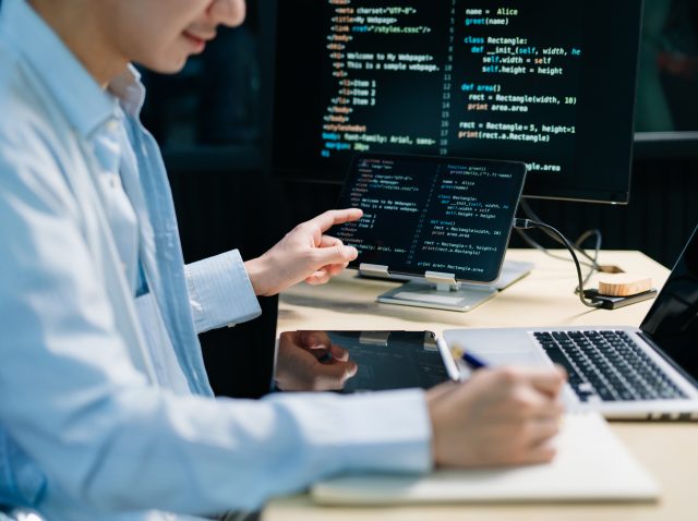 Asian software developer working late with code on screens, tabl Asian software developer working late with code on screens, tabl